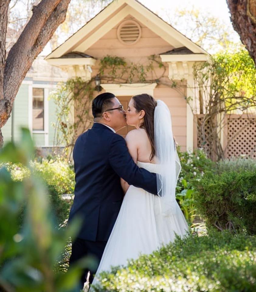 A bride and groom kissing outside in front of a charming gazebo at Heritage Square, Oxnard, surrounded by lush greenery.