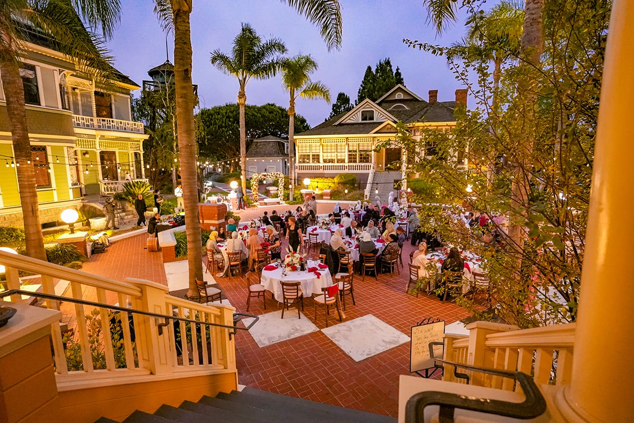 Elegant outdoor evening event at Heritage Square in Oxnard with guests seated at tables, surrounded by palm trees and warmly lit buildings.