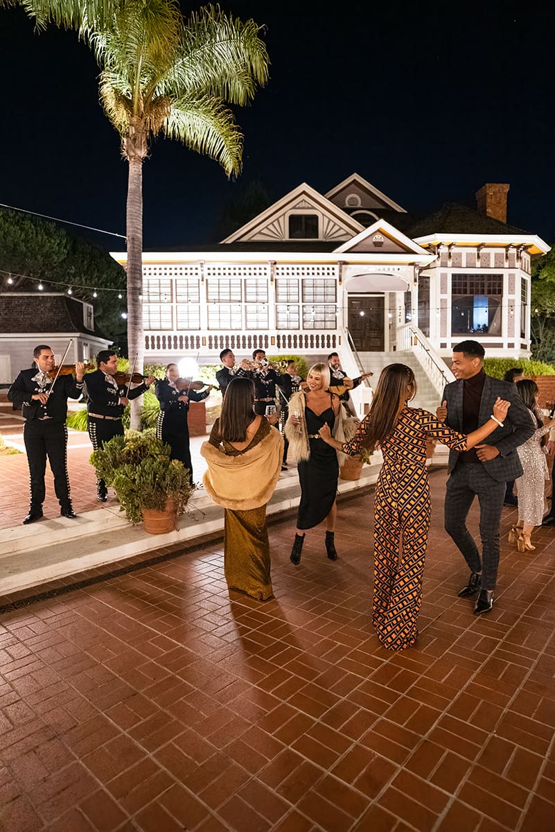 Guests dancing at an outdoor evening party at Heritage Square in Oxnard, with a live band playing, lit building and palm trees in the background.
