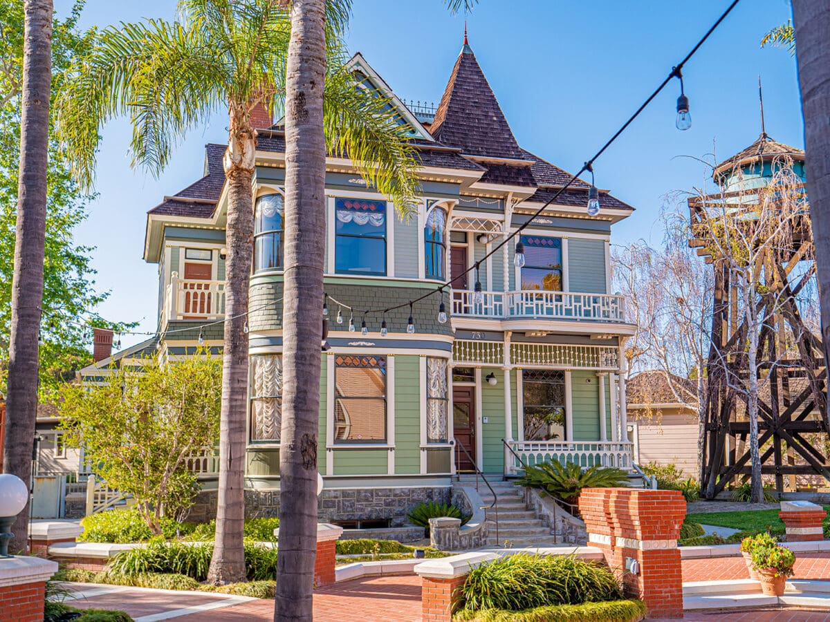 Victorian-style house with decorative trims, a tower, and surrounded by palm trees in Heritage Square Oxnard, under a clear blue sky.
