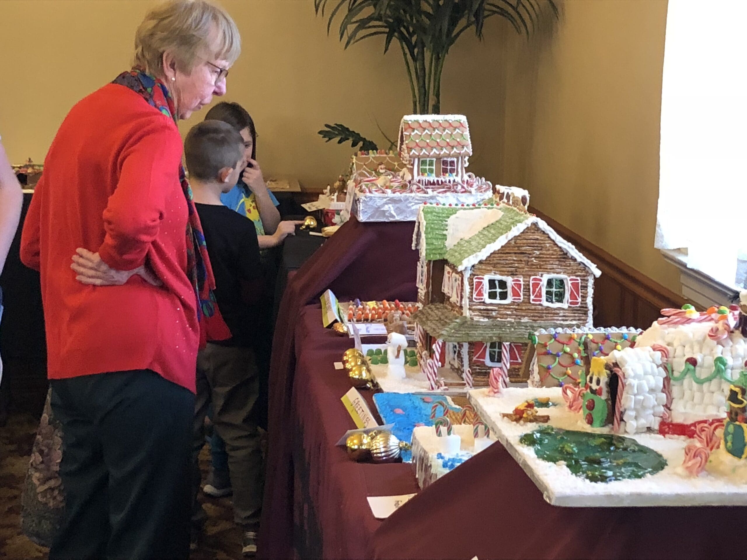 An older woman and a young boy examine gingerbread houses displayed on a table at an indoor event in Heritage Square, Oxnard.