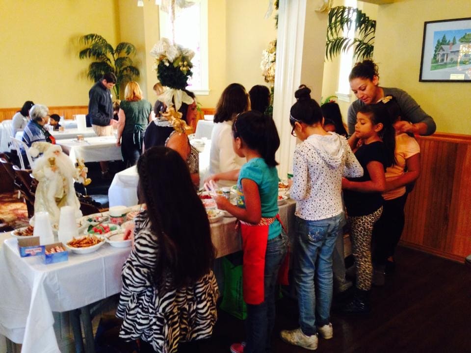 People of various ages queuing at a buffet table in Heritage Square, Oxnard, during a social event in a decorated room.