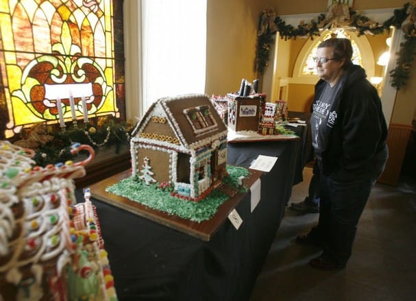 A person viewing gingerbread houses displayed on a table near a stained glass window in Heritage Square, Oxnard.